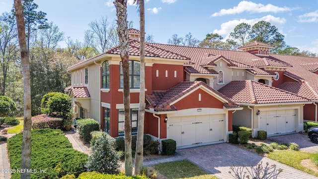 mediterranean / spanish-style house with stucco siding, a tile roof, decorative driveway, a garage, and a chimney