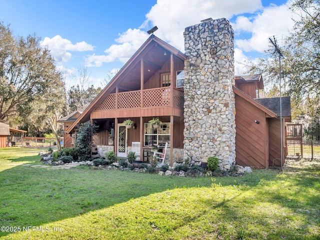 view of front of property with a balcony, a shingled roof, stone siding, a chimney, and a front yard