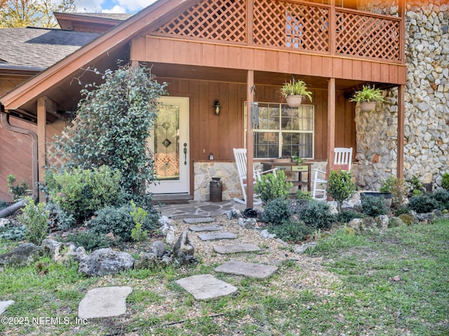 property entrance with stone siding, a shingled roof, and a porch