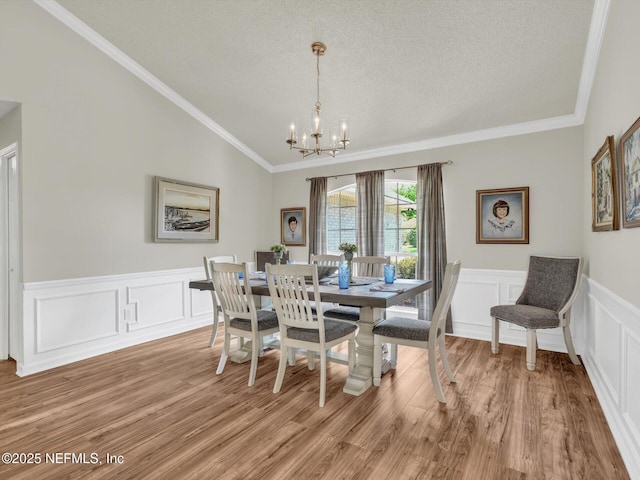 dining area featuring an inviting chandelier, vaulted ceiling, light wood finished floors, and a textured ceiling