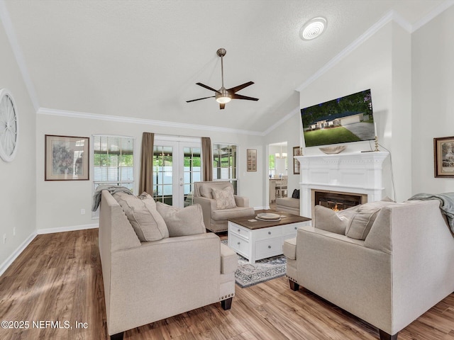 living room with a warm lit fireplace, ornamental molding, vaulted ceiling, french doors, and light wood-style floors