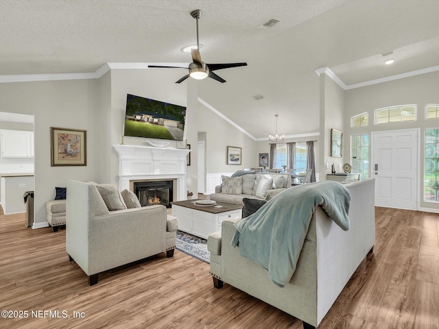 living area with a glass covered fireplace, visible vents, crown molding, and light wood-style flooring