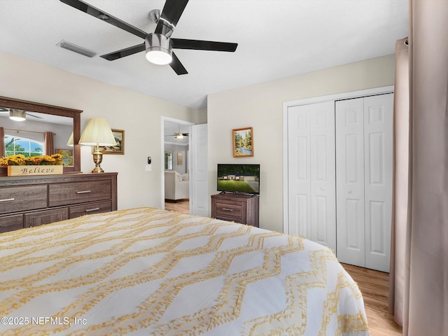 bedroom with light wood-type flooring, a ceiling fan, visible vents, and a closet