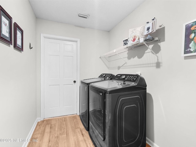 washroom with laundry area, light wood finished floors, visible vents, baseboards, and washer and clothes dryer