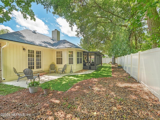 back of house featuring french doors, a patio, a chimney, a sunroom, and a fenced backyard