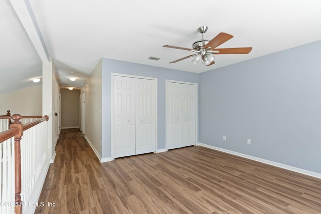 unfurnished bedroom with wood finished floors, a ceiling fan, baseboards, visible vents, and multiple closets