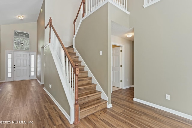 entryway with stairway, wood finished floors, a towering ceiling, and baseboards