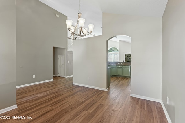 unfurnished dining area with dark wood-style floors, baseboards, arched walkways, and a chandelier