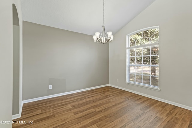 spare room featuring a chandelier, lofted ceiling, baseboards, and wood finished floors