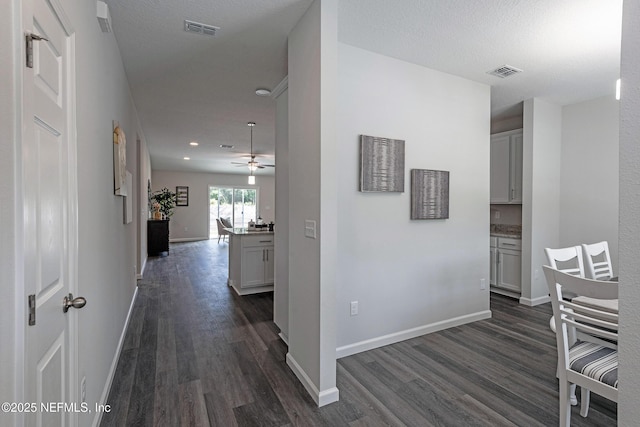 corridor with dark wood-type flooring, visible vents, and baseboards