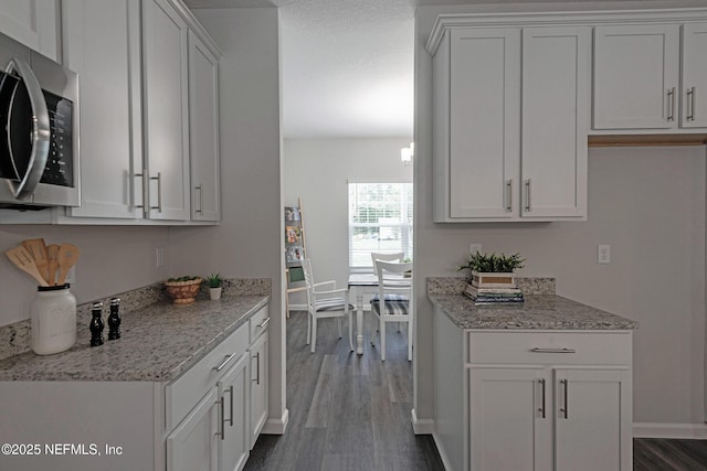 kitchen featuring baseboards, white cabinets, dark wood-style floors, stainless steel microwave, and light stone counters