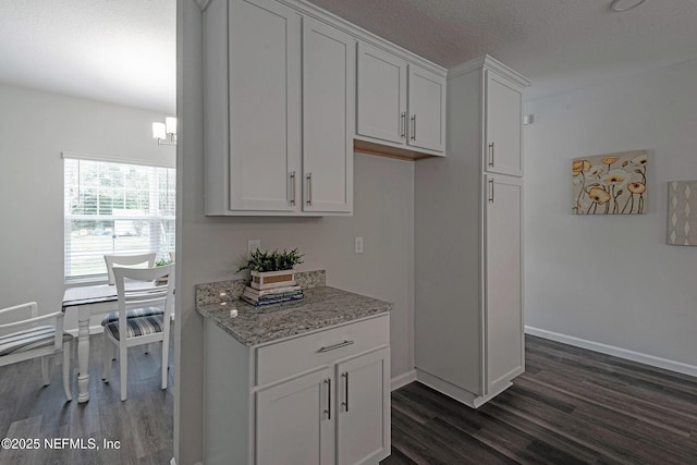 kitchen featuring baseboards, dark wood-type flooring, white cabinetry, and light stone countertops