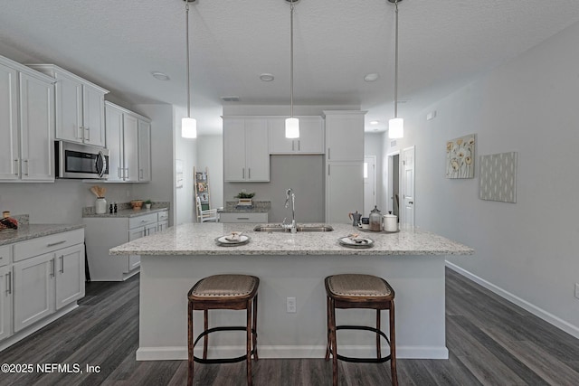 kitchen with dark wood-style floors, stainless steel microwave, a sink, and a center island with sink