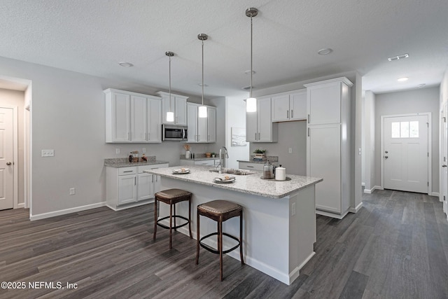 kitchen with a kitchen island with sink, dark wood-style flooring, a sink, white cabinetry, and stainless steel microwave