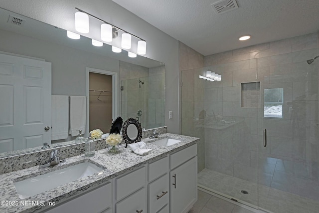 full bathroom featuring a stall shower, a walk in closet, visible vents, and a sink