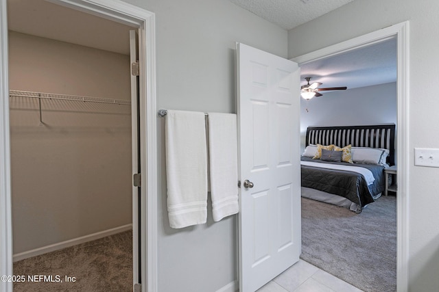 bedroom featuring a textured ceiling, light tile patterned floors, light colored carpet, a ceiling fan, and baseboards