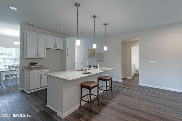 kitchen with a sink, visible vents, white cabinetry, dark wood-style floors, and a center island with sink