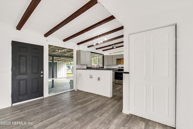 kitchen with beam ceiling, stainless steel electric stove, dark countertops, a sink, and wood finished floors