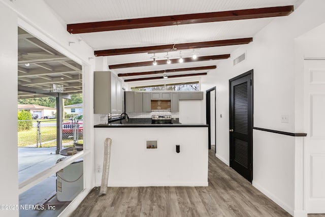 kitchen with wood finished floors, a sink, decorative backsplash, beamed ceiling, and dark countertops