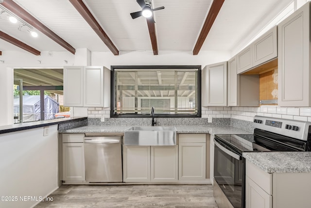 kitchen with stainless steel appliances, a sink, backsplash, light wood finished floors, and beamed ceiling