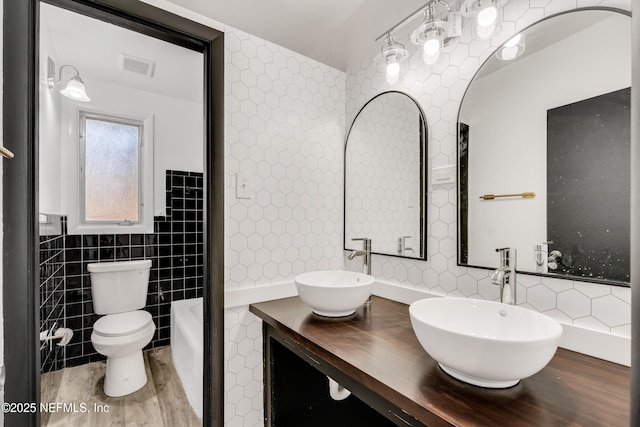 bathroom with toilet, visible vents, tile walls, and a sink