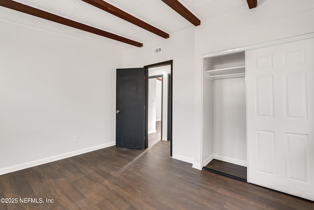 unfurnished bedroom with a closet, dark wood-style flooring, baseboards, and beam ceiling