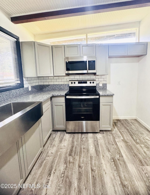 kitchen with decorative backsplash, light wood-style flooring, gray cabinets, stainless steel appliances, and beam ceiling