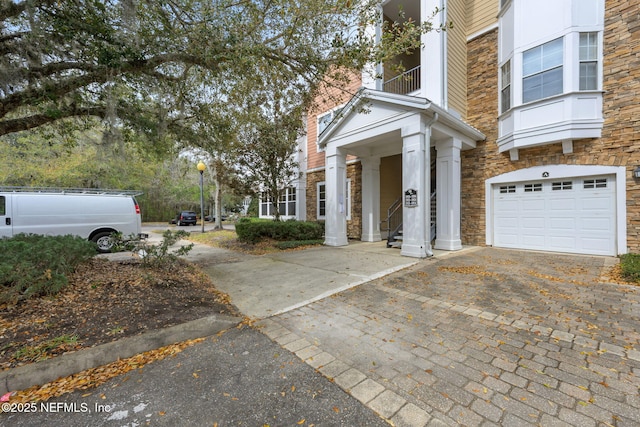 view of property exterior with a garage, stone siding, decorative driveway, and a balcony