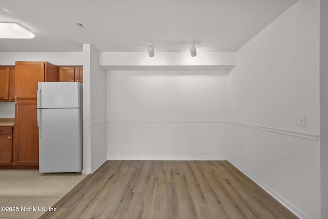 kitchen with baseboards, light wood finished floors, freestanding refrigerator, and brown cabinets