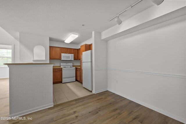 kitchen featuring white appliances, baseboards, light wood-style flooring, brown cabinets, and a peninsula