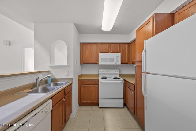 kitchen with white appliances, light tile patterned floors, brown cabinetry, and a sink