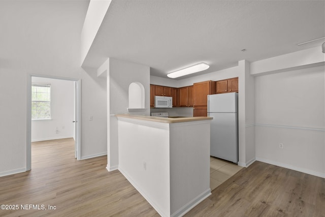 kitchen with baseboards, white appliances, light wood-style floors, and brown cabinets