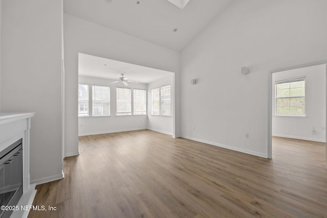 unfurnished living room with baseboards, wood finished floors, a wealth of natural light, and a glass covered fireplace