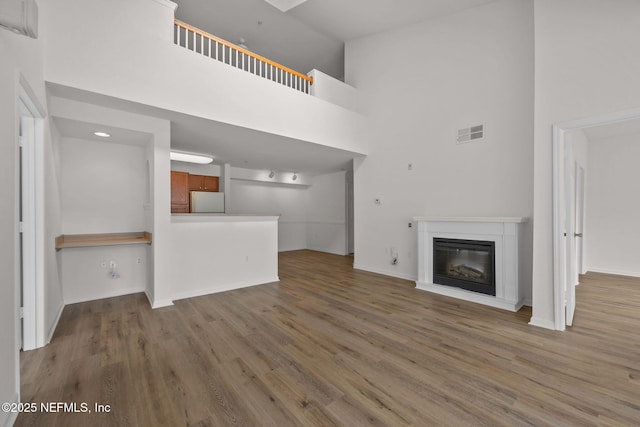 unfurnished living room featuring a glass covered fireplace, a high ceiling, wood finished floors, and visible vents