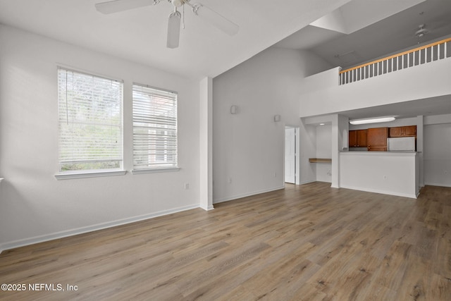 unfurnished living room with high vaulted ceiling, light wood-type flooring, ceiling fan, and baseboards