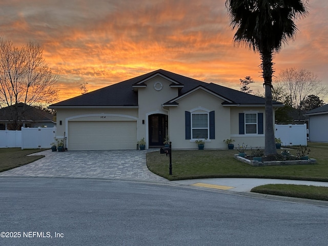 ranch-style home featuring decorative driveway, an attached garage, fence, and a yard