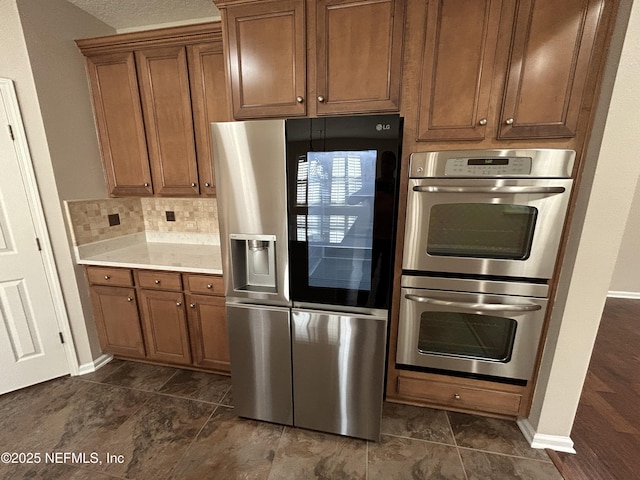 kitchen with brown cabinetry, baseboards, stainless steel appliances, light countertops, and tasteful backsplash