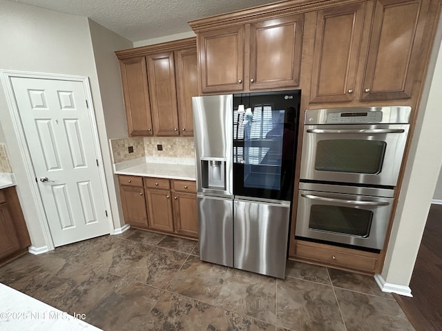 kitchen featuring a textured ceiling, appliances with stainless steel finishes, brown cabinetry, and light countertops