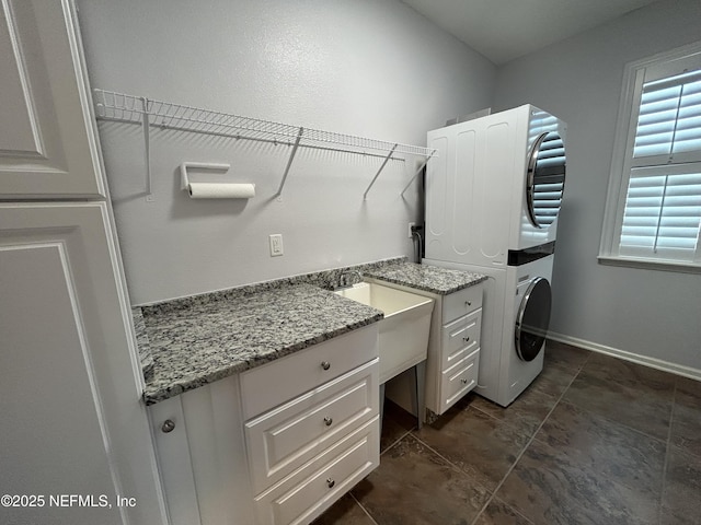 clothes washing area with laundry area, stacked washer and clothes dryer, and baseboards