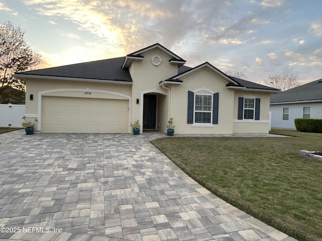 ranch-style house featuring a front lawn, decorative driveway, an attached garage, and stucco siding