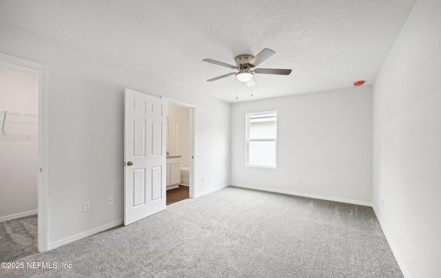 unfurnished bedroom featuring carpet, baseboards, a spacious closet, and a textured ceiling