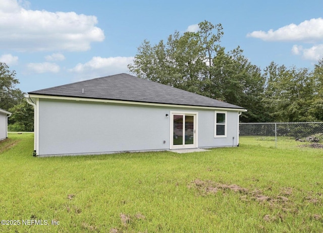 rear view of property featuring a yard, fence, and stucco siding