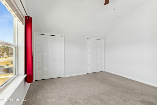 unfurnished bedroom featuring carpet floors, a ceiling fan, baseboards, vaulted ceiling, and two closets