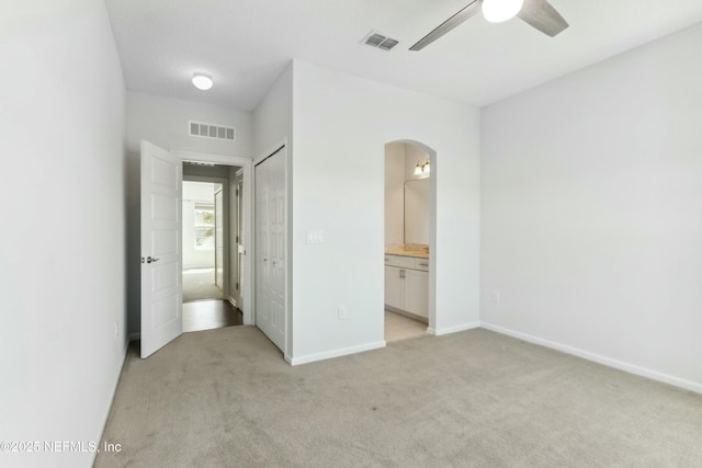 unfurnished bedroom featuring visible vents, arched walkways, and light colored carpet