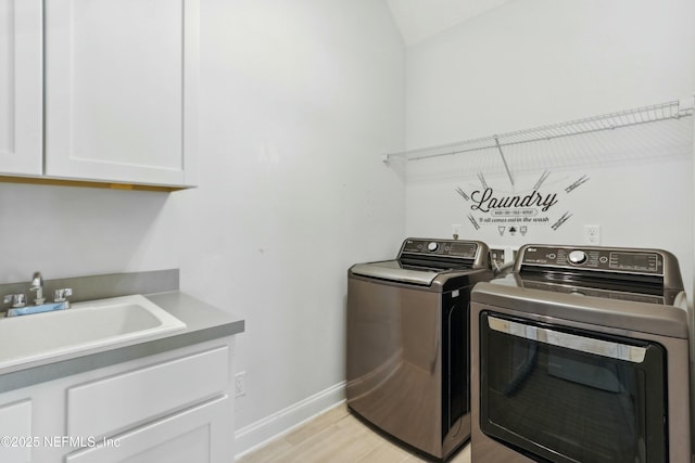 laundry room with cabinet space, light wood finished floors, baseboards, washer and clothes dryer, and a sink