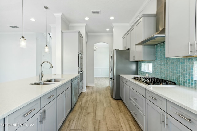 kitchen with arched walkways, a sink, visible vents, appliances with stainless steel finishes, and wall chimney exhaust hood