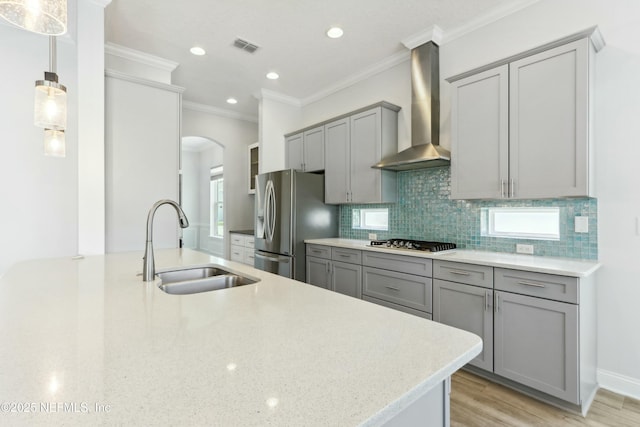 kitchen with stainless steel appliances, gray cabinets, backsplash, a sink, and wall chimney exhaust hood