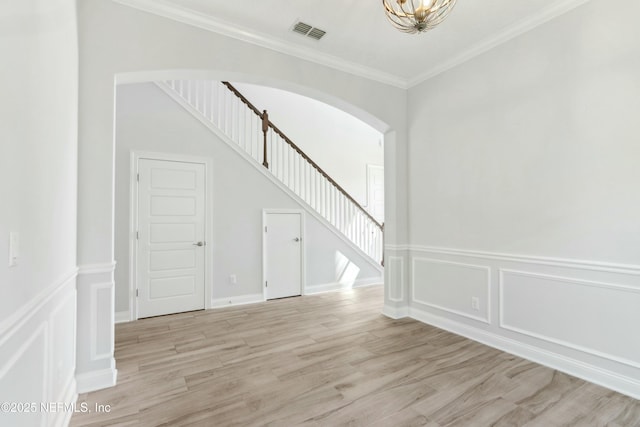 spare room with visible vents, arched walkways, light wood-style flooring, ornamental molding, and stairs