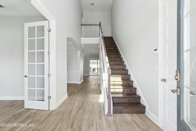 stairway featuring arched walkways, wood finished floors, visible vents, and baseboards