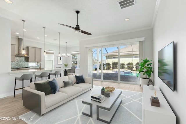 living room featuring light wood-style floors, visible vents, crown molding, and ceiling fan